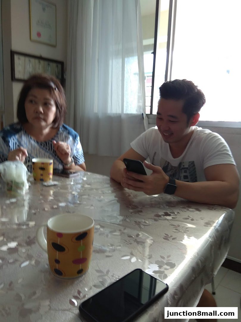 Two people sitting at a table with mugs and phones, one person is looking at their phone.
