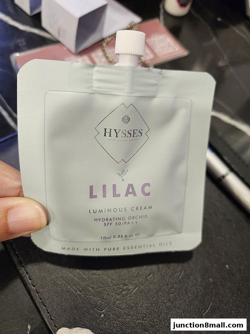 A hand holds a sample packet of HYSSES LILAC Luminous Cream.