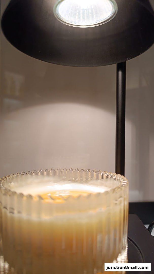 A close-up of a candle in a decorative glass jar, lit by a spotlight.