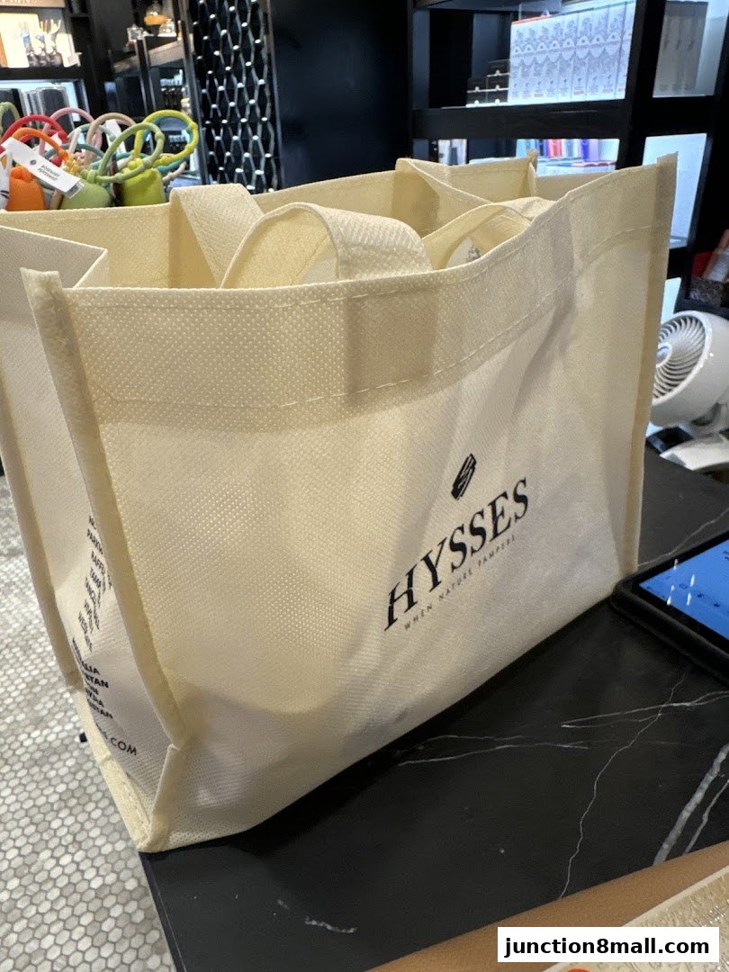 A cream-colored tote bag with the HYSSES logo sits on a black marble surface.