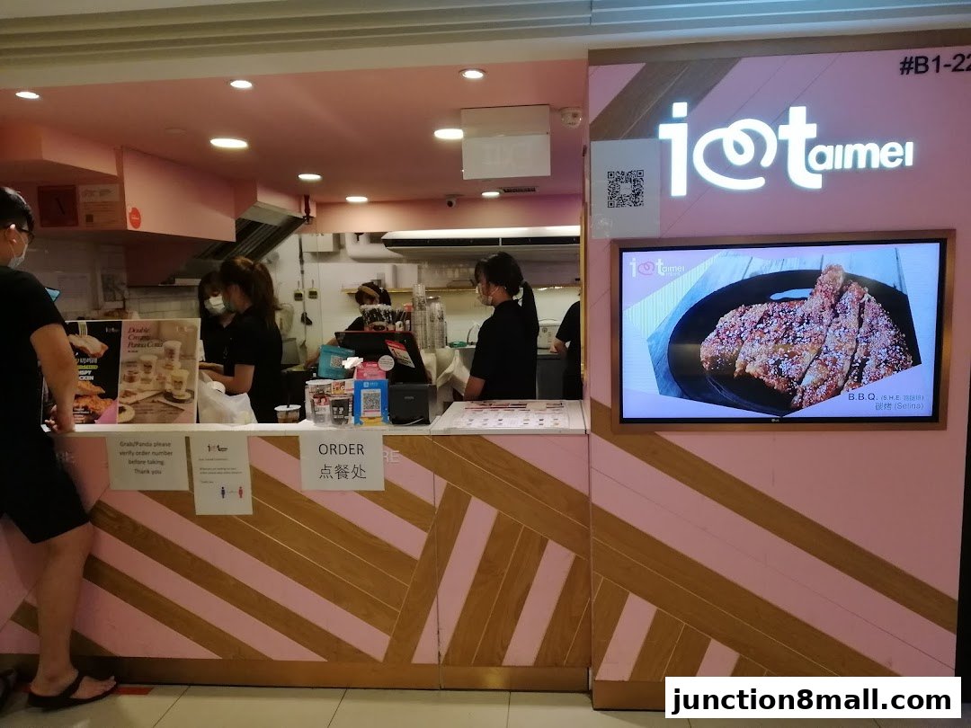 A brightly lit shop counter with staff serving customers and a display of fried chicken.