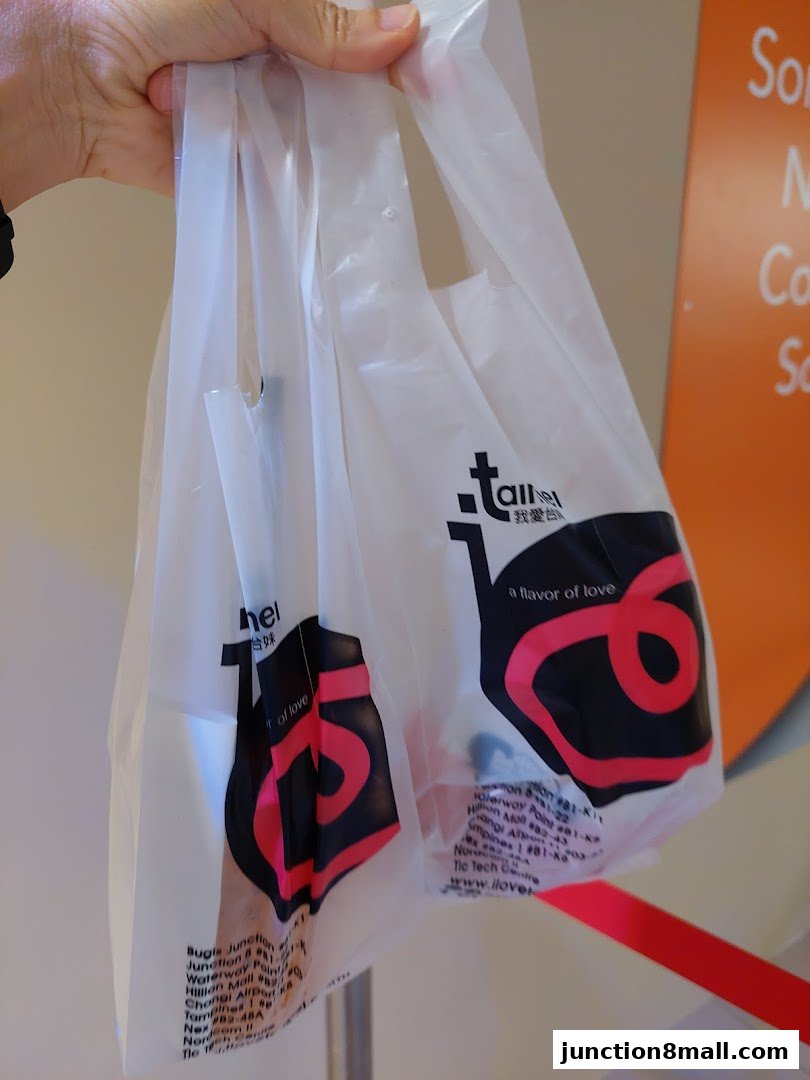 A hand holds two white plastic shopping bags with the 'I Love Taimei' logo.