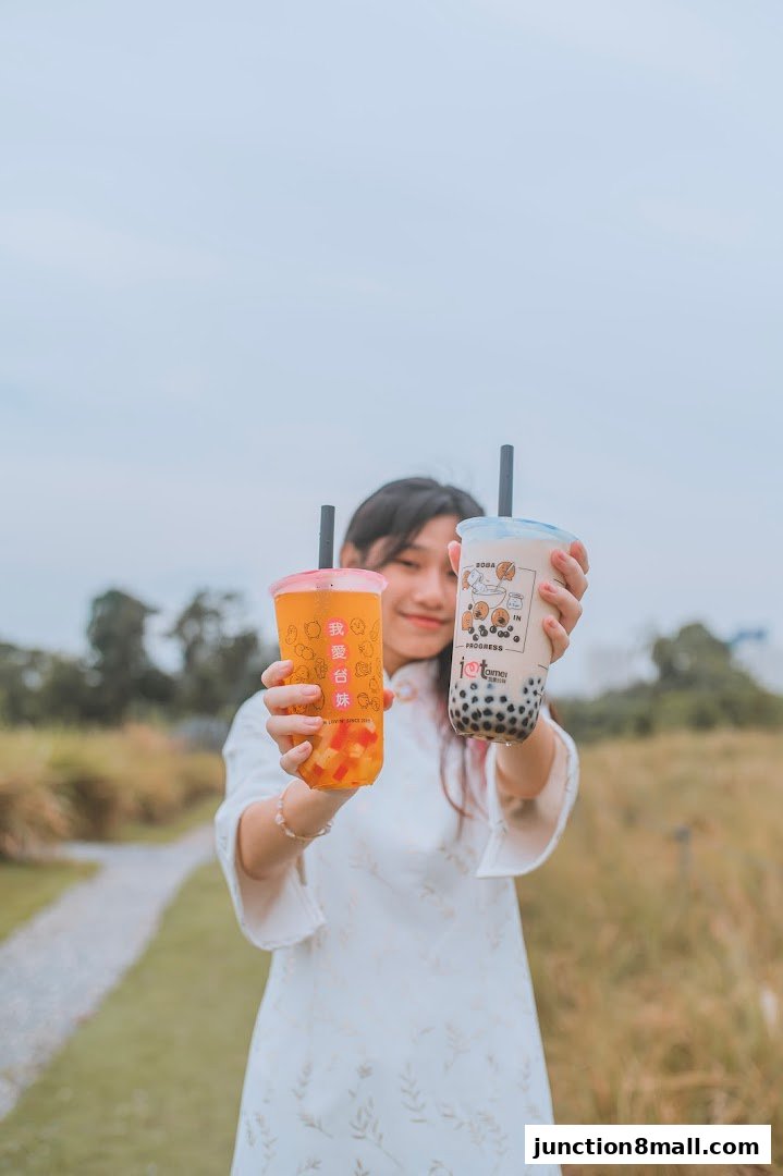A young woman in a white dress holds up two bubble tea drinks, one orange and one milky.