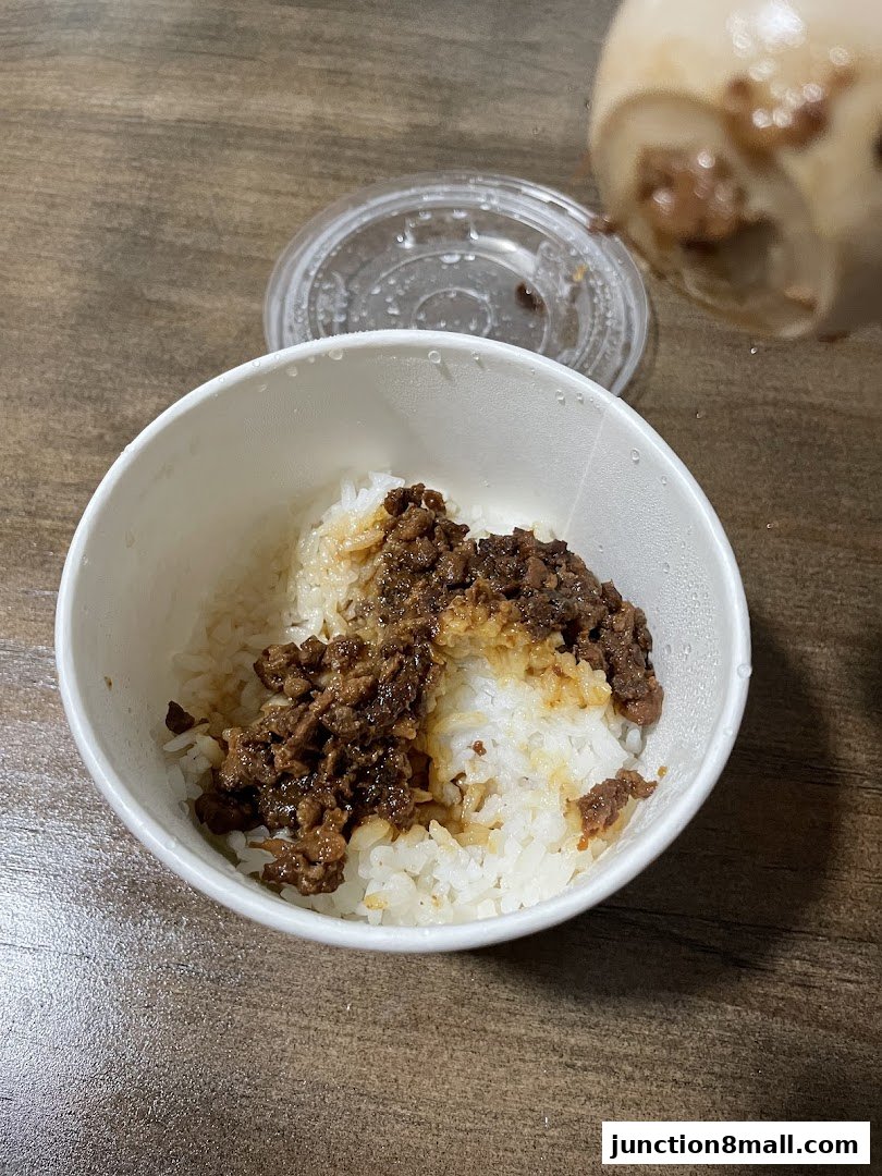 A bowl of white rice topped with savory minced meat and sauce, with a lid nearby.