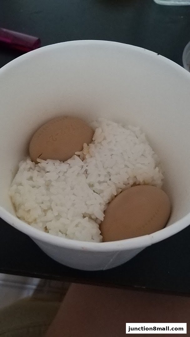 A white cup filled with white rice and three brown eggs.