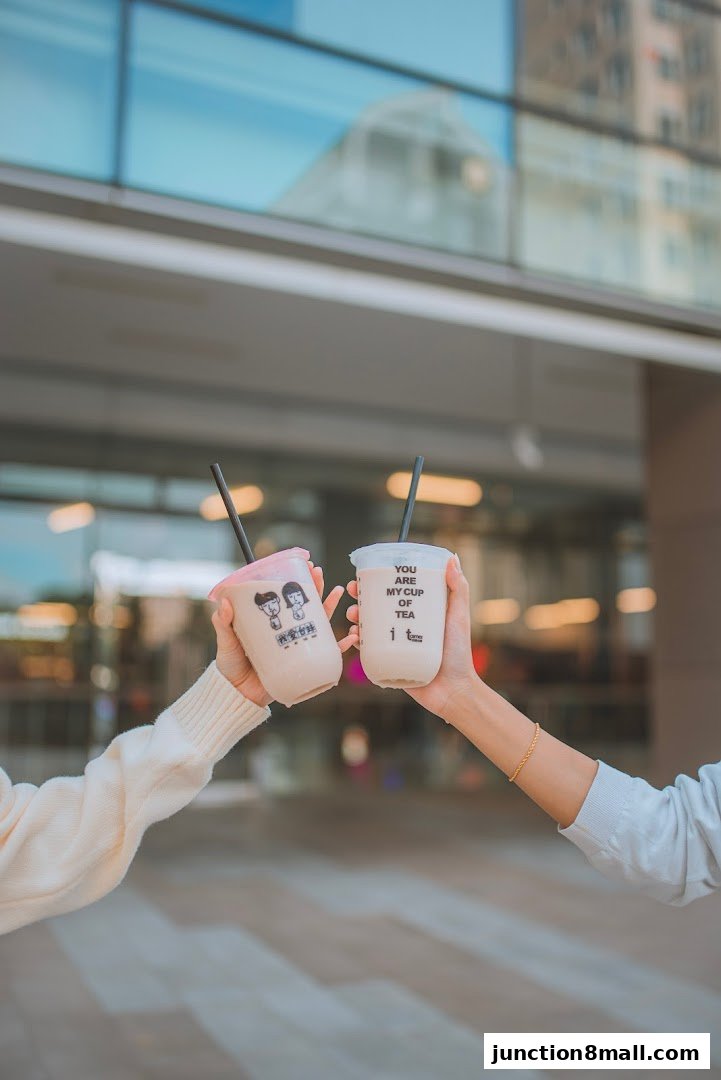 Two hands holding bubble tea cups with the shop's logo and branding.
