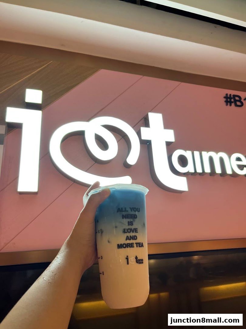 A hand holds a bubble tea with a blue and white gradient in front of a shop sign.