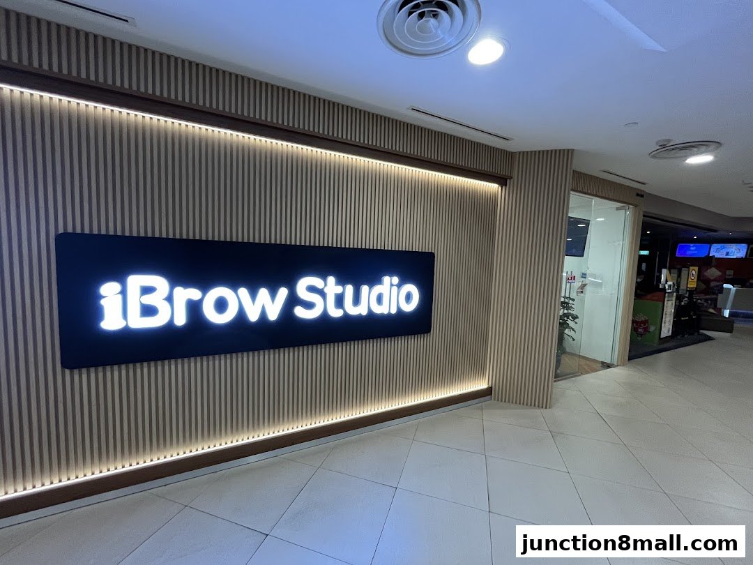 The illuminated sign for iBrow Studio is mounted on a slatted wooden wall.