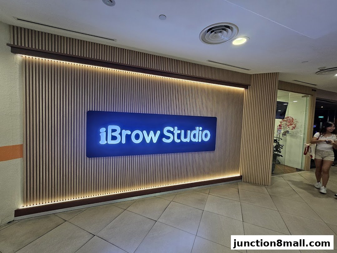 The illuminated sign for iBrow Studio is mounted on a slatted wooden wall.