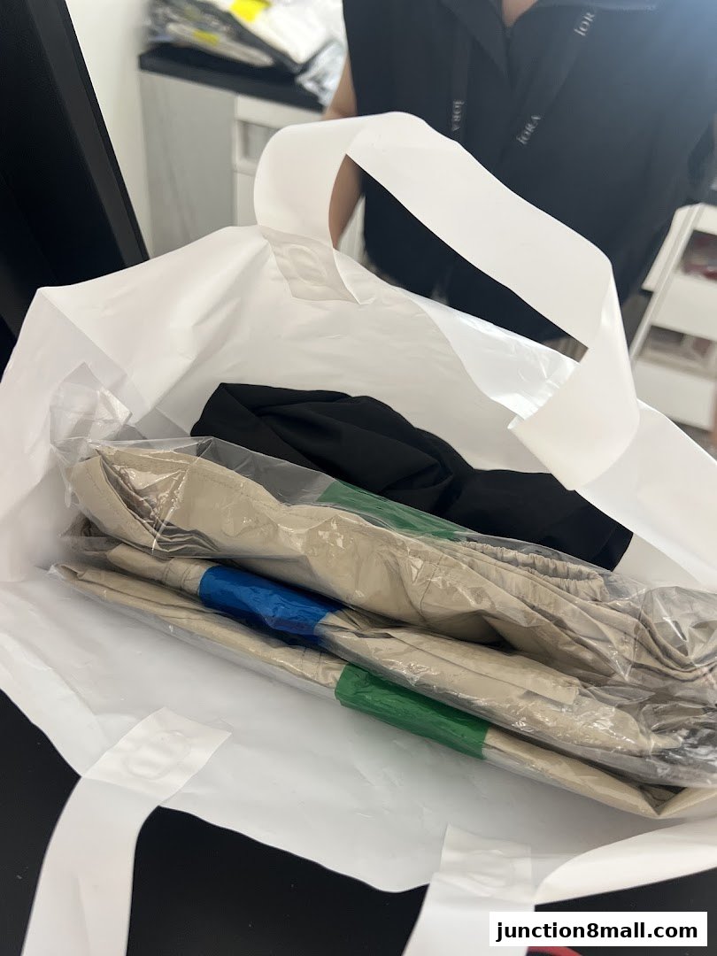 A shopping bag filled with neatly folded clothes, including pants with colored stripes.