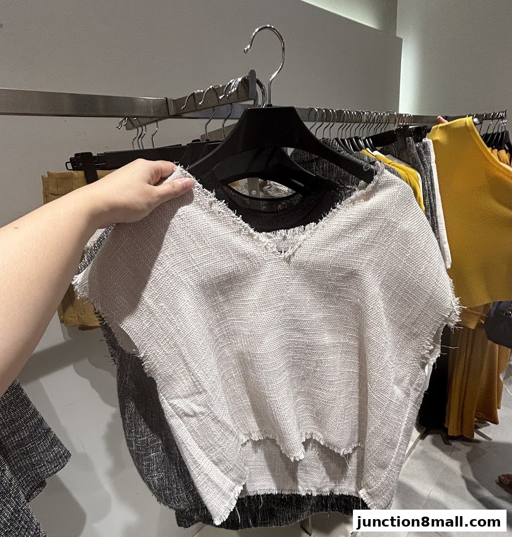 A hand holds up a textured white top with frayed edges, showcasing new arrivals.