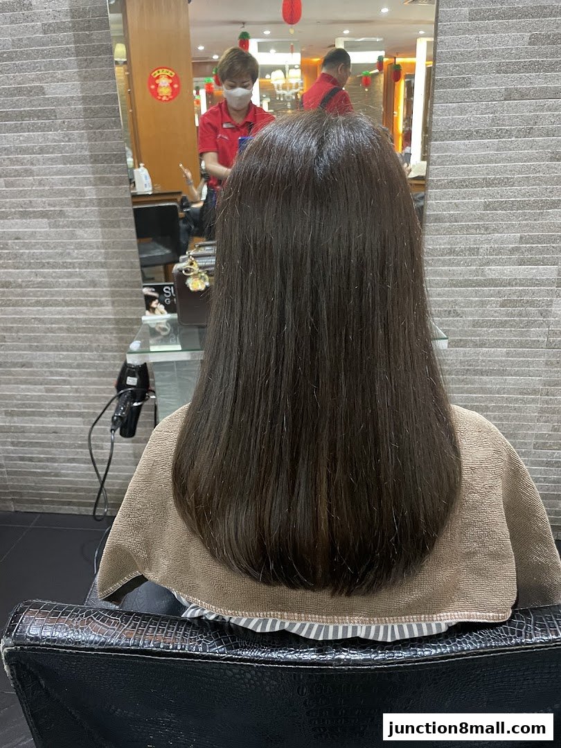 A person's back with long, dark hair is shown in a salon chair, with stylists reflected in the mirror.