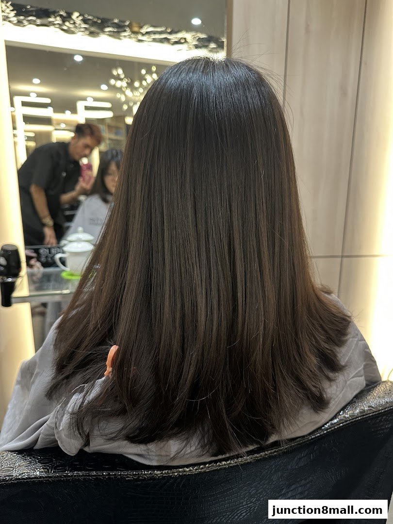 A person's back with long, dark, layered hair in a salon chair.
