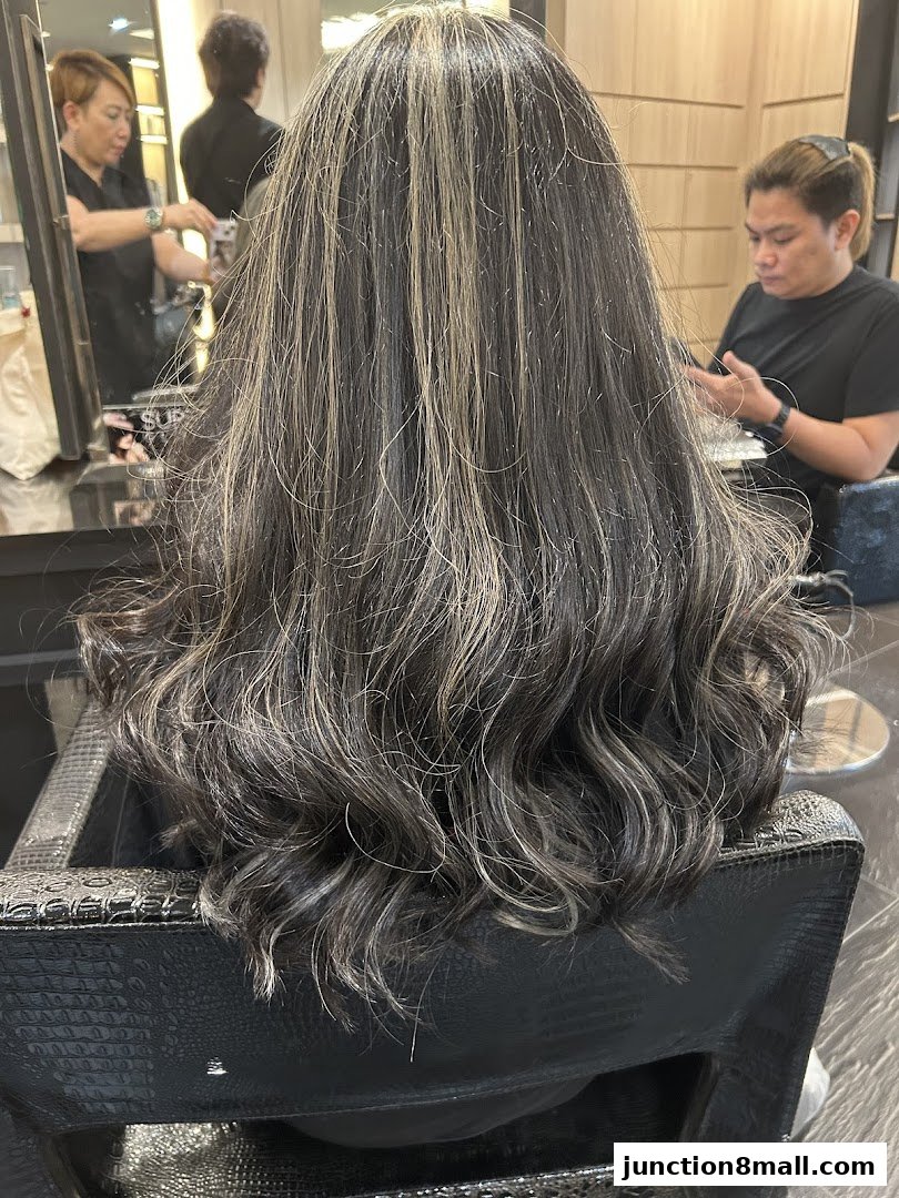 A person's back with styled, highlighted hair in a salon chair.