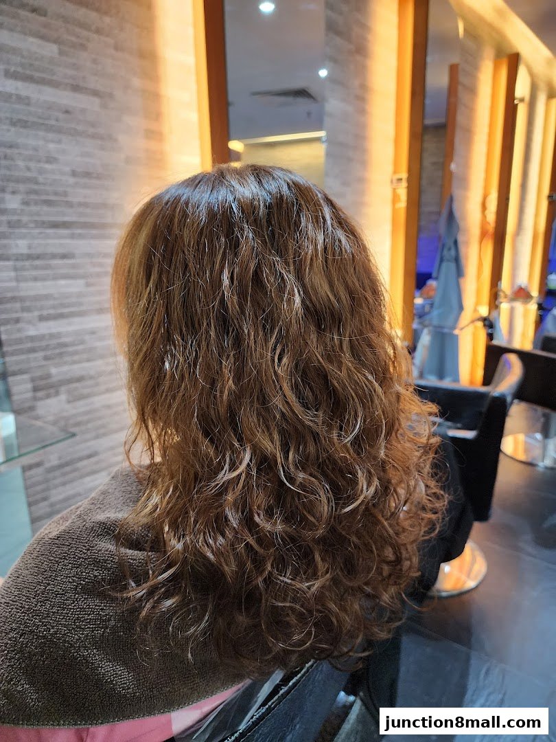 A person's back with freshly permed, curly brown hair in a salon.