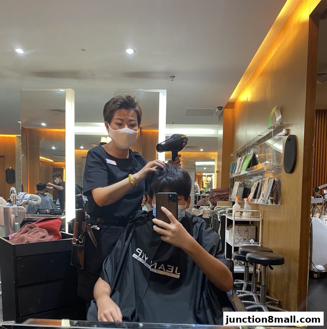 A hairstylist dries a client's hair while the client takes a mirror selfie.