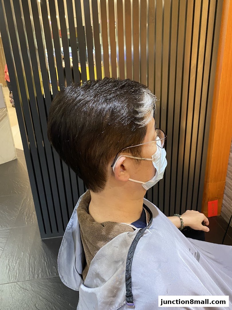 A person with short, dark hair with white highlights, wearing glasses and a mask, is getting their hair done.