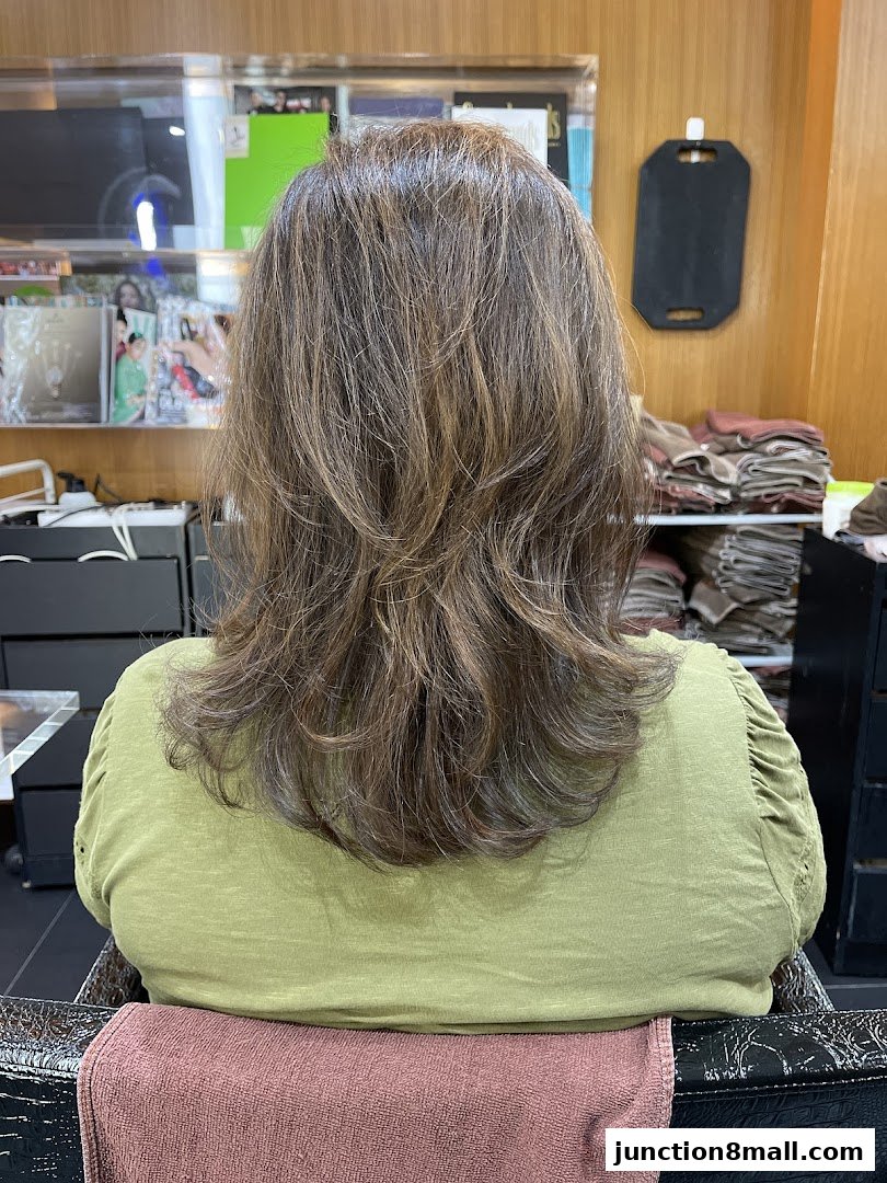A person with layered brown hair sitting in a salon chair, viewed from behind.