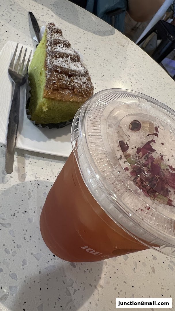 A slice of green cake with coconut and a drink with rose petals.
