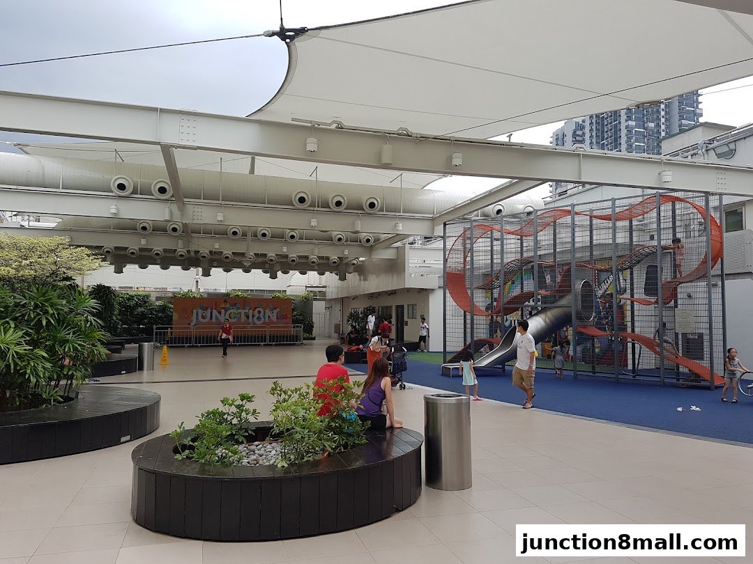 A rooftop playground with climbing structures and slides, under a large canopy.