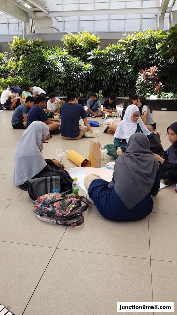 A group of young people sitting in a circle on the floor, with lush greenery in the background.