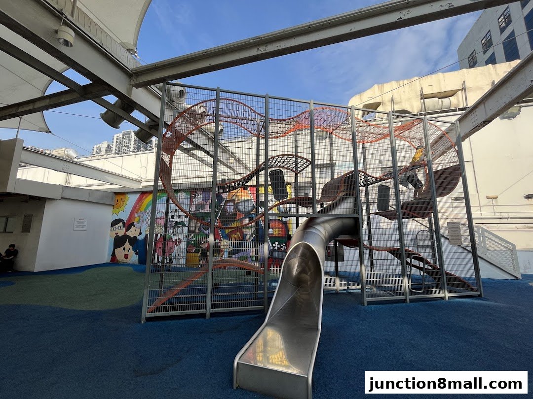 A colorful playground with a large climbing structure and slide, featuring vibrant murals on the wall.