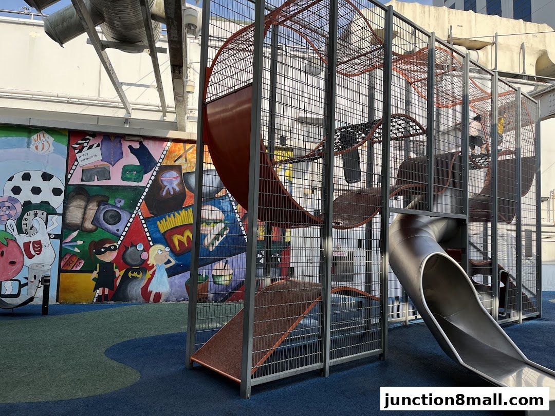 A colorful playground with a large metal slide and a vibrant mural on the wall.