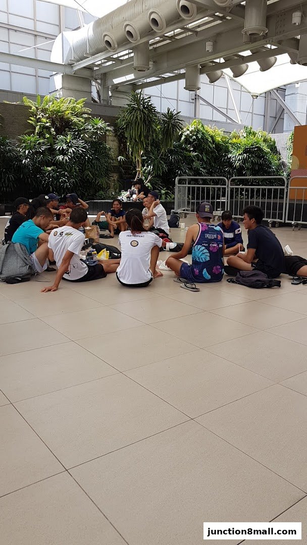 A group of people are sitting in a circle on the floor, surrounded by lush greenery.