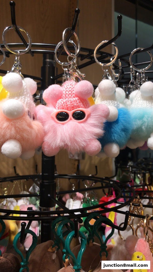 A display of colorful, fluffy pom-pom keychains with sunglasses and knitted hats.
