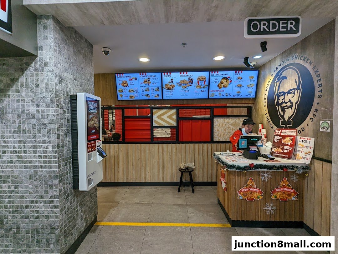 KFC counter with digital menus, a staff member, and Christmas decorations.