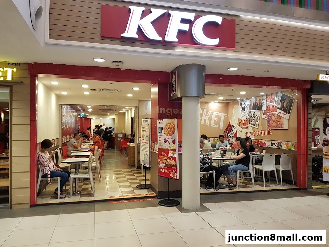 KFC restaurant interior with customers dining and a prominent KFC logo above the entrance.