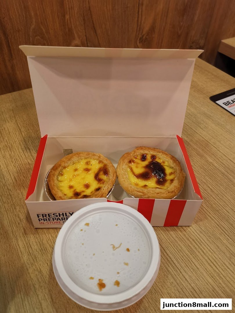 Two golden-brown egg tarts in a KFC branded box with a white lid.