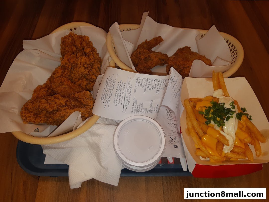 A tray of KFC fried chicken, cheese fries, and a drink on a wooden table.