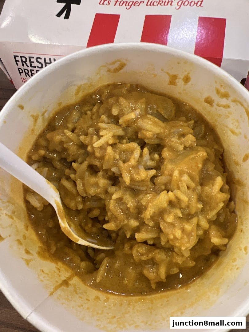 A close-up of a bowl of KFC curry rice with a white spoon.