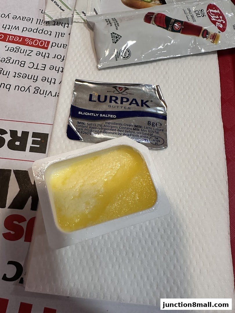 A close-up of a single-serving butter portion and chili sauce packet from KFC.