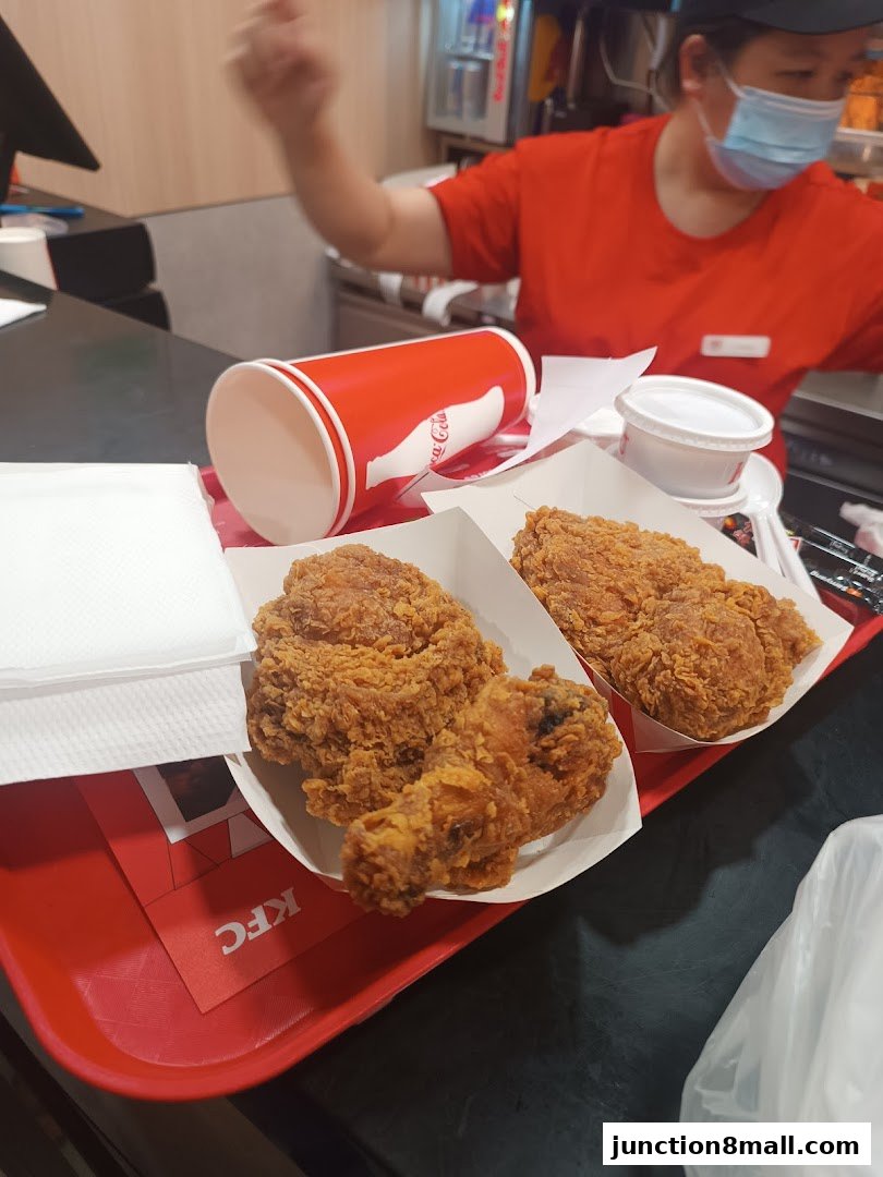 A tray of KFC fried chicken with a Coca-Cola cup and a masked employee in the background.