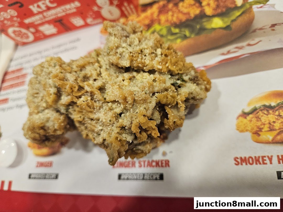 Close-up of crispy fried chicken with menu items from KFC in the background.