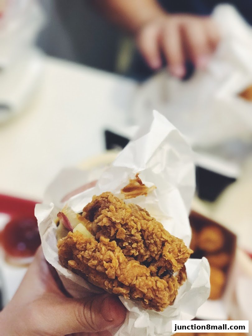 A hand holds a delicious piece of crispy fried chicken wrapped in paper.