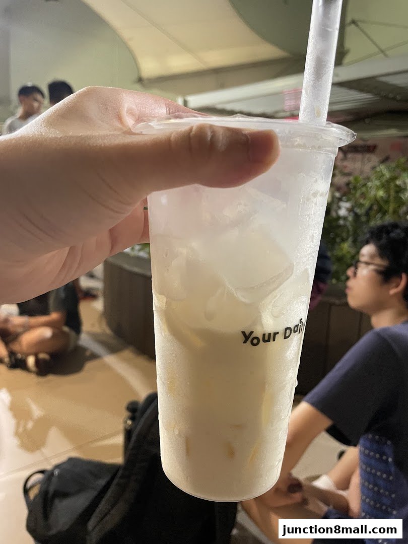 A hand holds a refreshing beverage from KOI Thé, with people in the background.