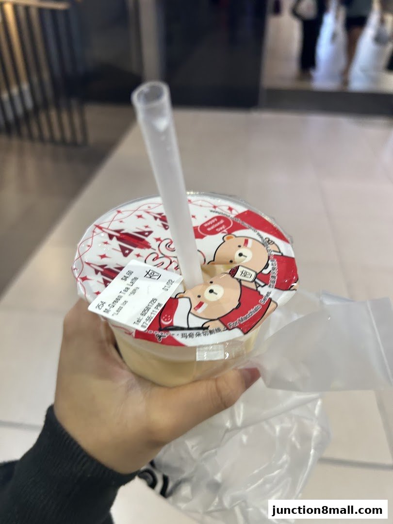 A hand holds a KOI Thé M-Green Tea Latte with a cute bear design on the lid.