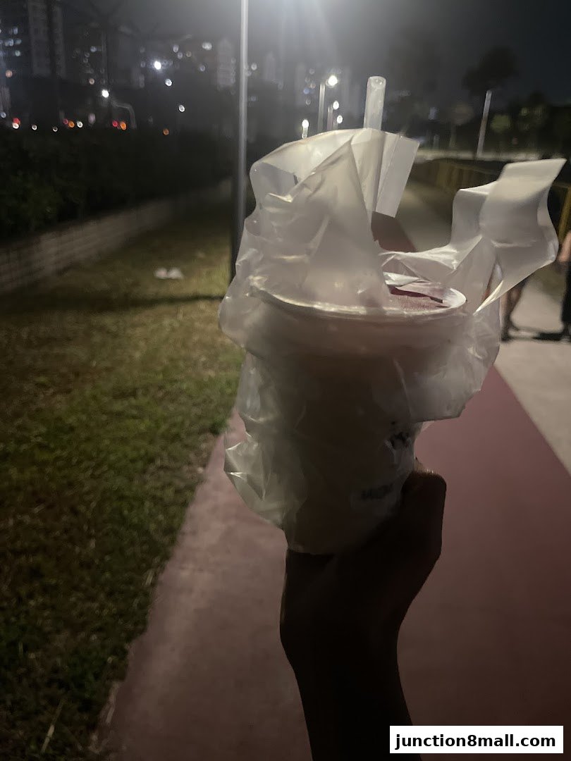 A hand holds a bubble tea drink in a plastic bag at night.