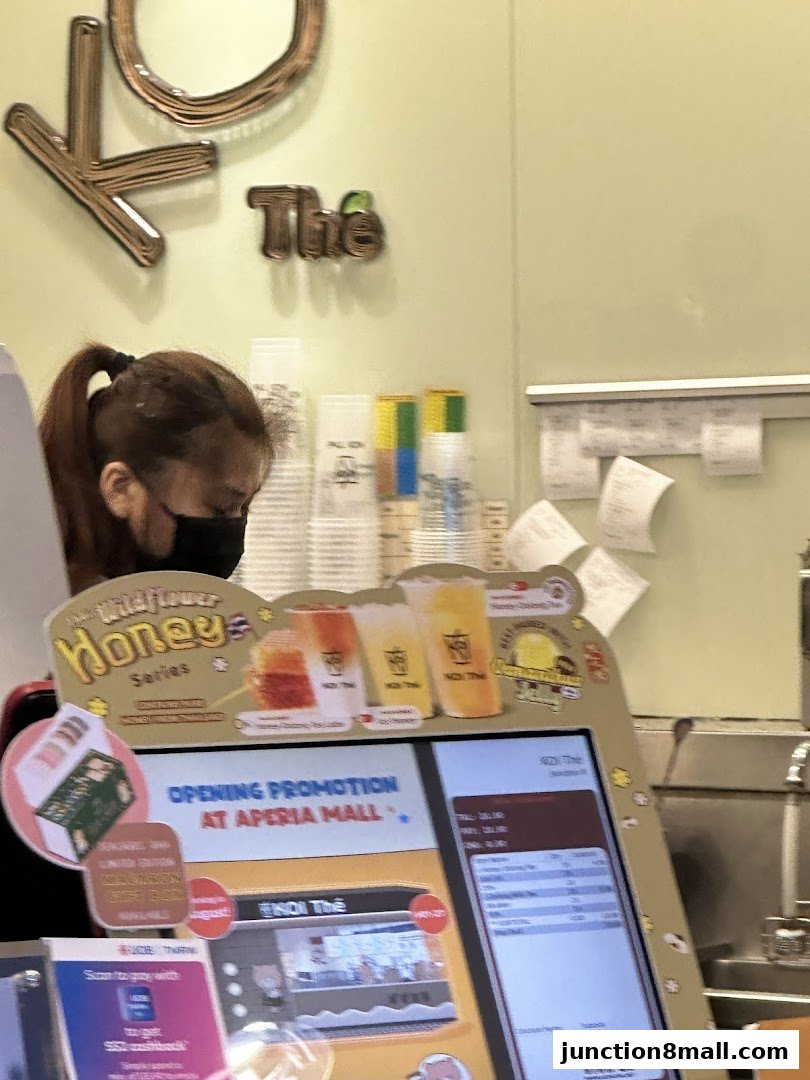 A person wearing a mask at a KOI Thé counter with drinks and a digital menu.