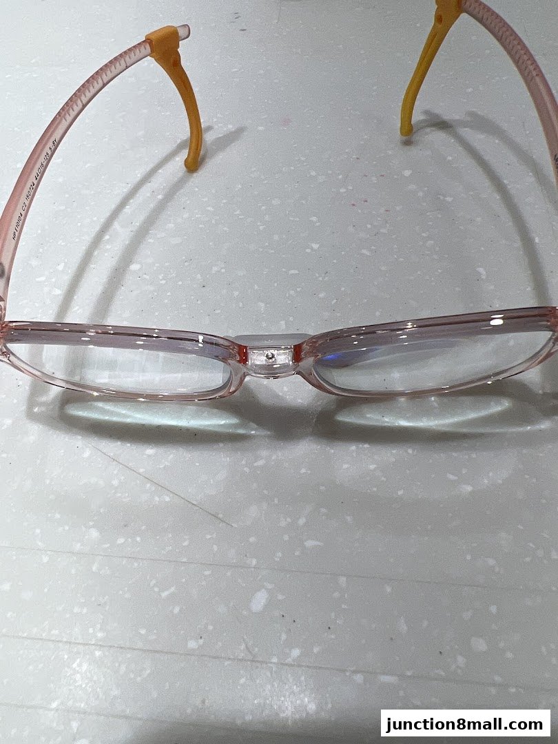 A pair of pink eyeglasses with yellow ear hooks rests on a speckled surface.