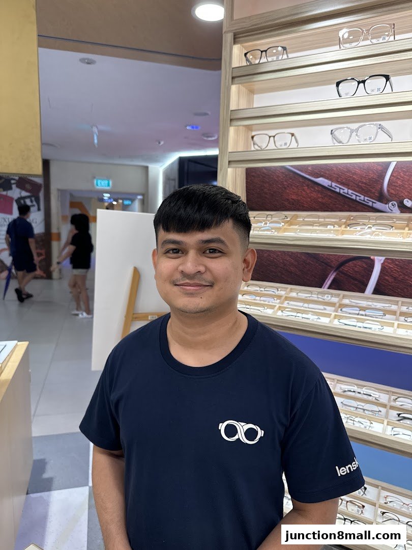 A man wearing a Lenskart t-shirt stands in front of a display of eyeglasses.