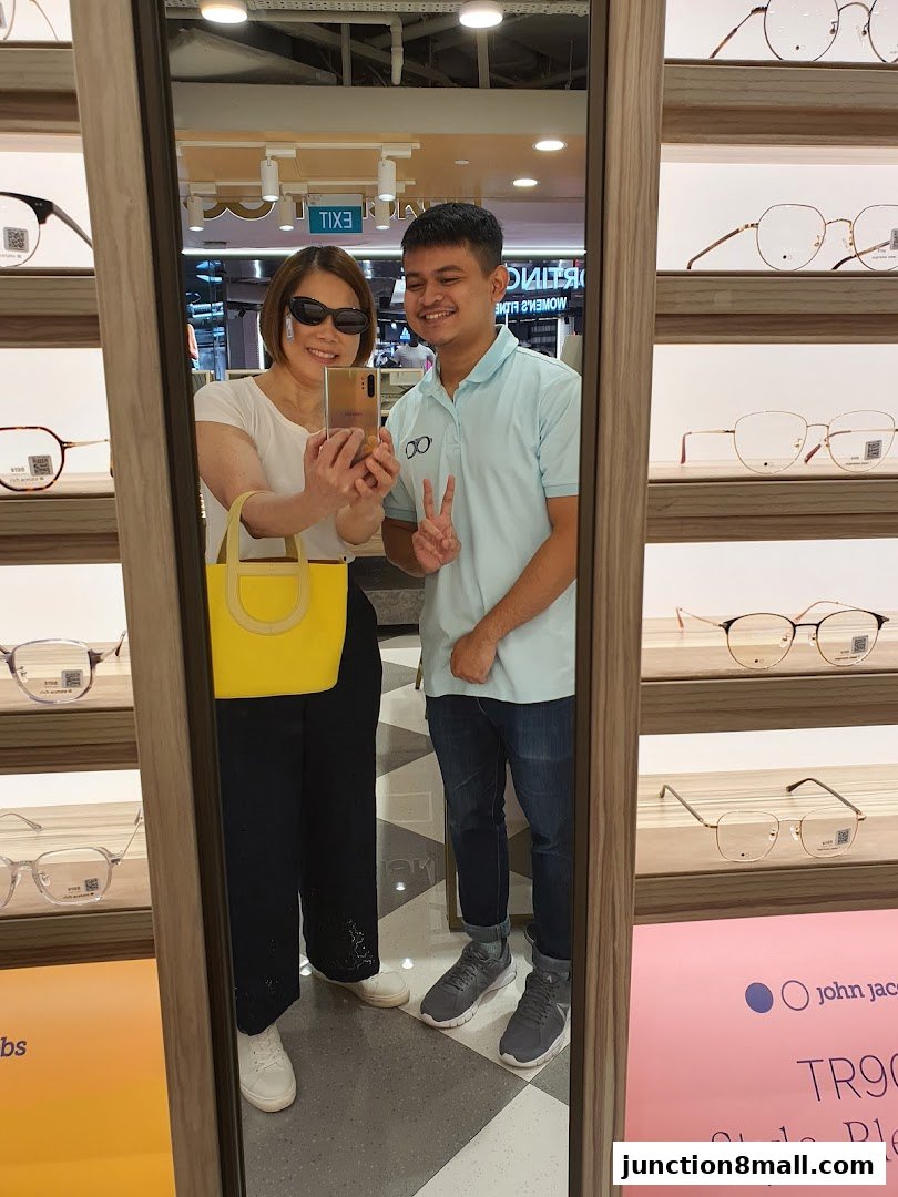 A woman and a man take a mirror selfie in an optical shop, surrounded by eyeglasses.