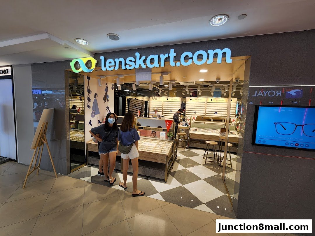 Two women stand outside a Lenskart store, which displays various eyeglasses and a promotional screen.