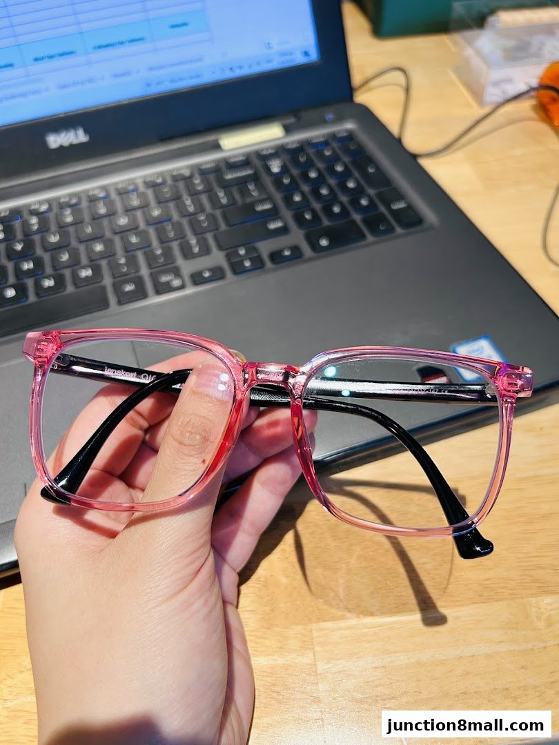 A hand holds pink-framed glasses in front of a laptop with a spreadsheet on the screen.