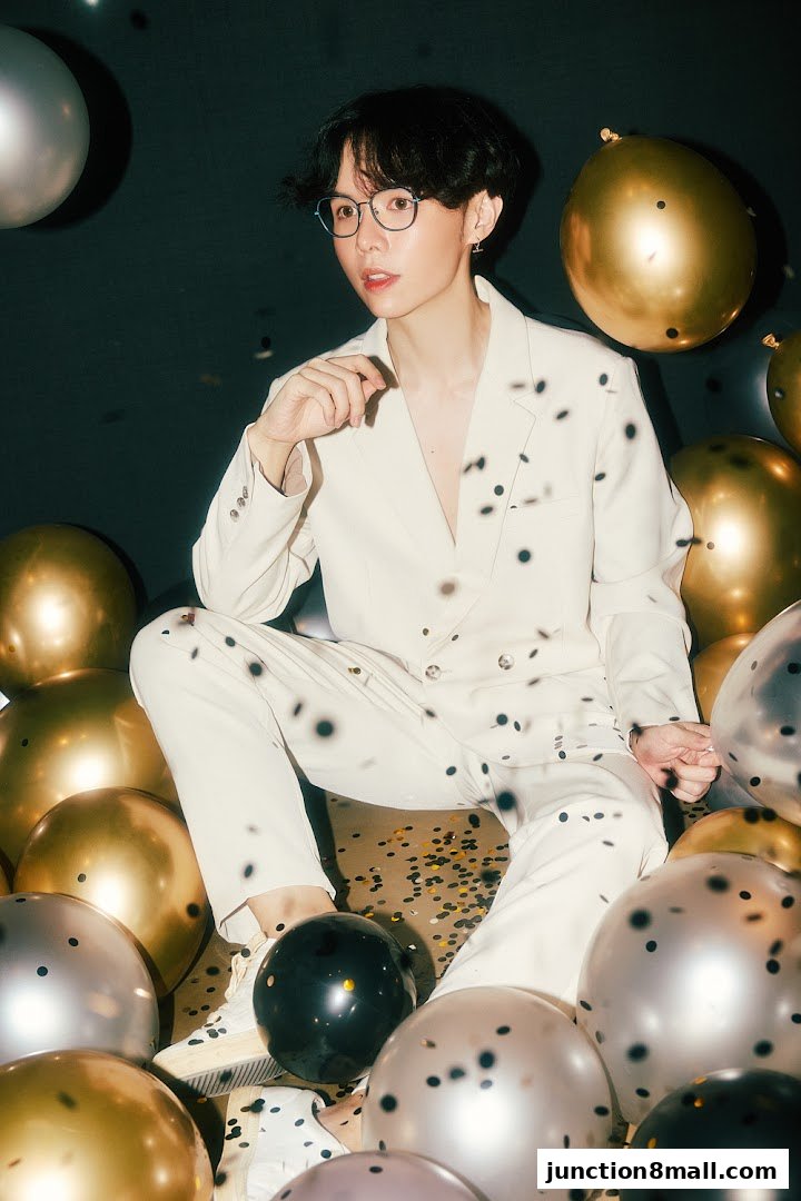 A person in a cream suit sits surrounded by balloons and confetti.