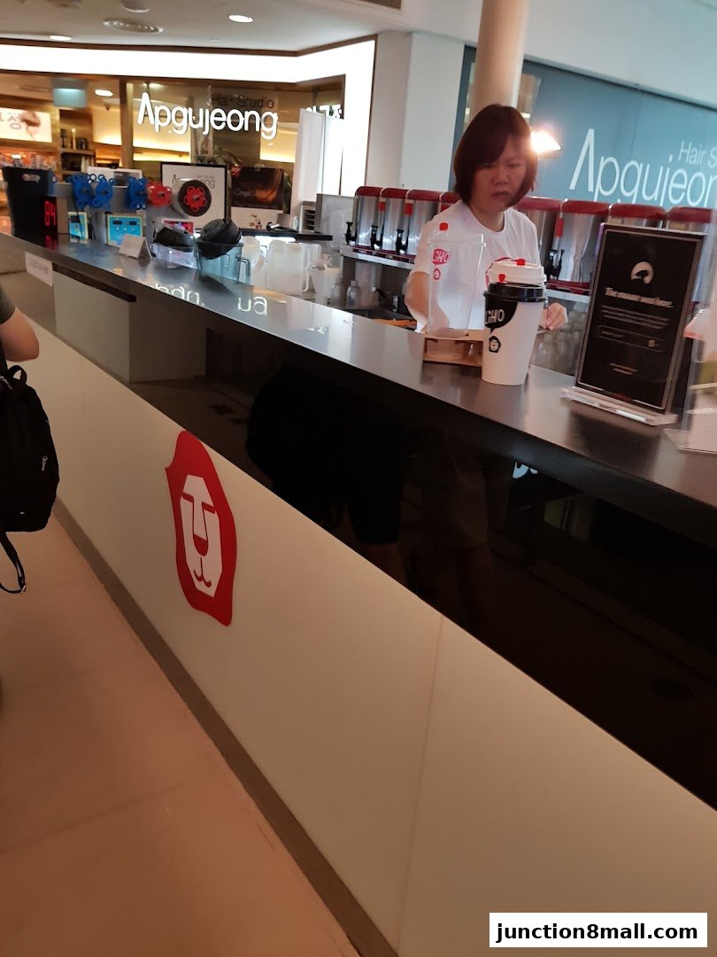 A LiHO TEA staff member prepares drinks behind a counter with branded cups.