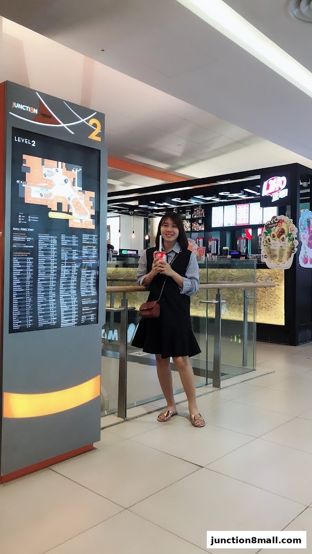 A woman holds a drink in front of a LiHO TEA shop and a mall directory.